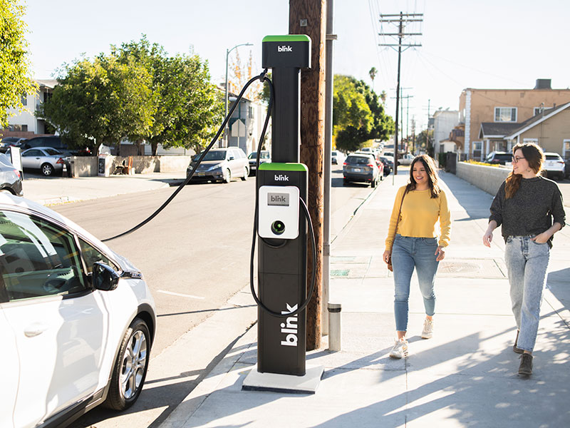 Two young women approaching their EV using a Blink charging