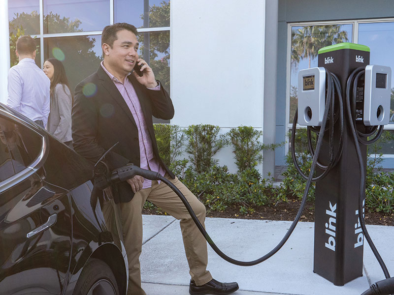 EV Charging System Installation, man charging electric vehicle while on his phone